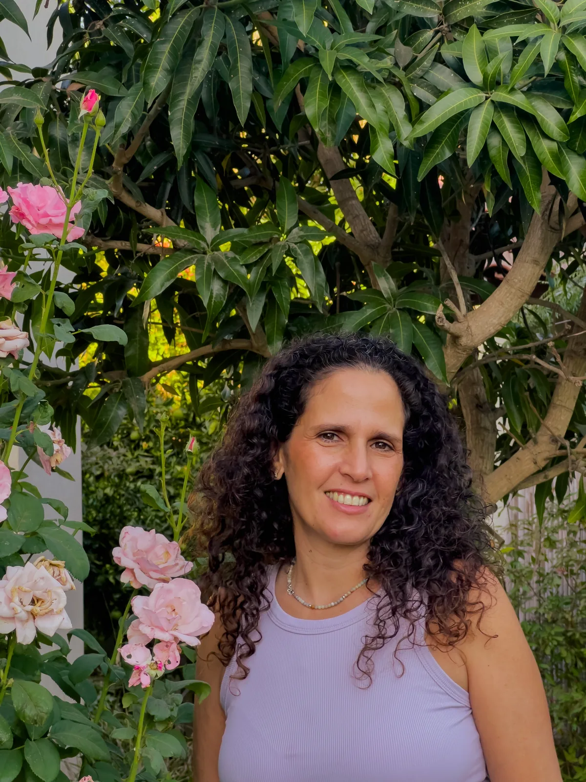 קרן זהר פאר מחייכת בגינה, לצד ורדים ורודים